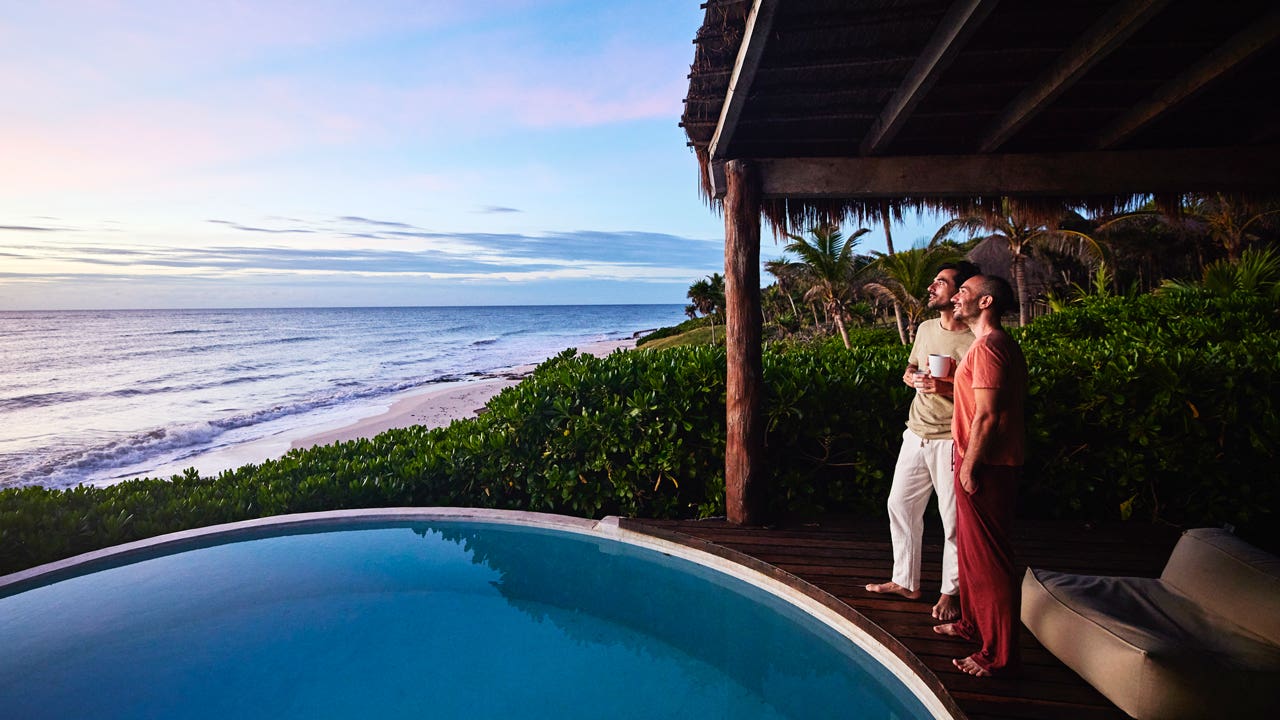 couple standing poolside watching sunrise at luxury tropical villa overlooking beach and ocean