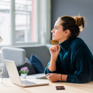 woman holding credit card and working on laptop while looking out the window