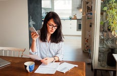 Woman looks through bills at a kitchen table