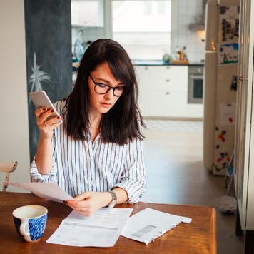 Woman looks through bills at a kitchen table