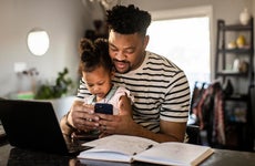 Father with daughter in his lap while looking at phone