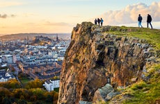 Group of people walking along cliff edge looking at Edinburgh city views