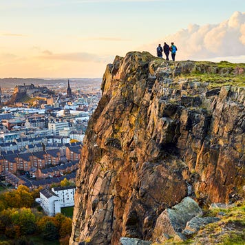Group of people walking along cliff edge looking at Edinburgh city views