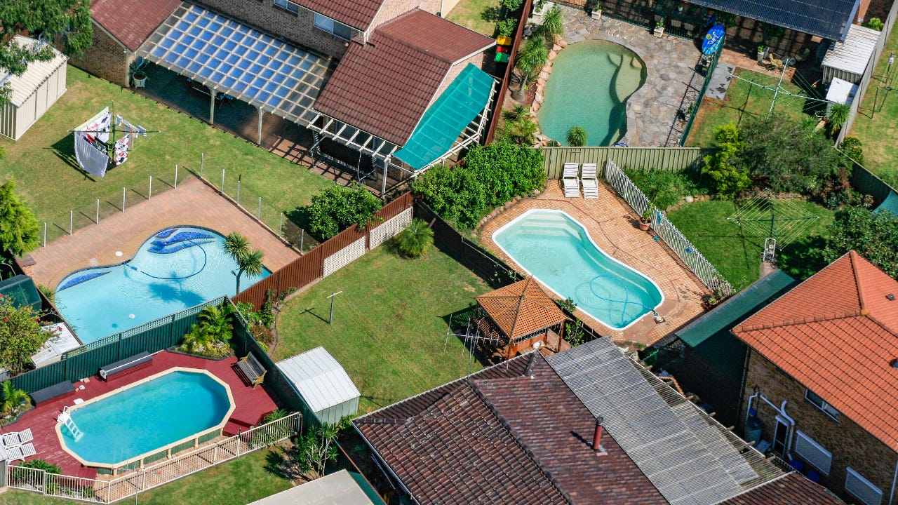 Aerial view of suburban backyards. Four pools in different styles are visible.