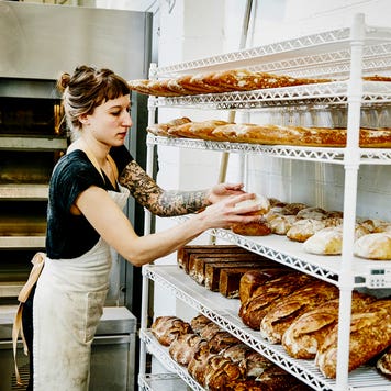 female baker placing bread to cool on a rack in bakery
