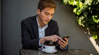 man sitting at outdoor cafe table and looking at his phone