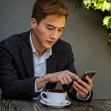 man sitting at outdoor cafe table and looking at his phone