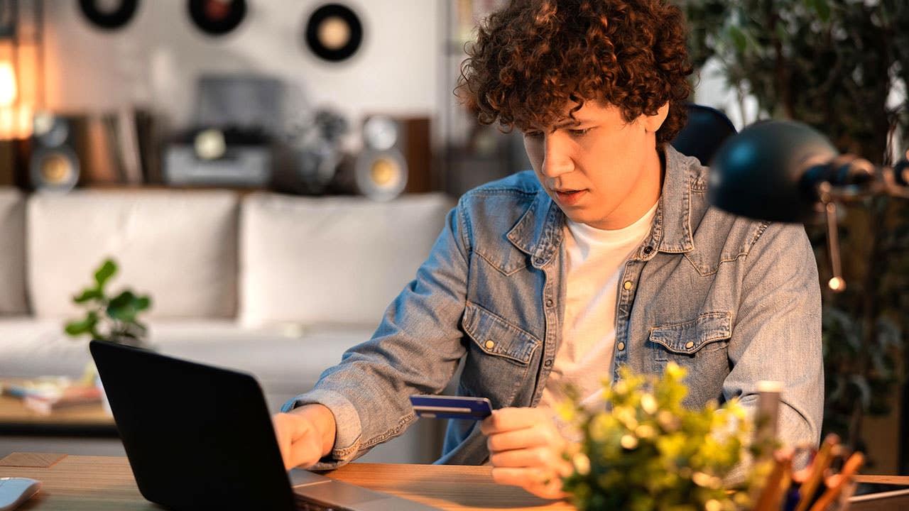 a young man at home holding a credit card and using a computer