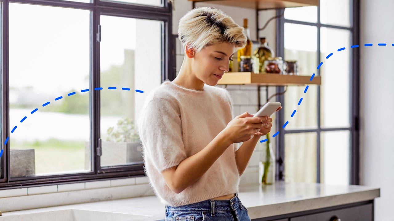 young woman standing in kitchen and looking at her phone