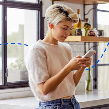 young woman standing in kitchen and looking at her phone