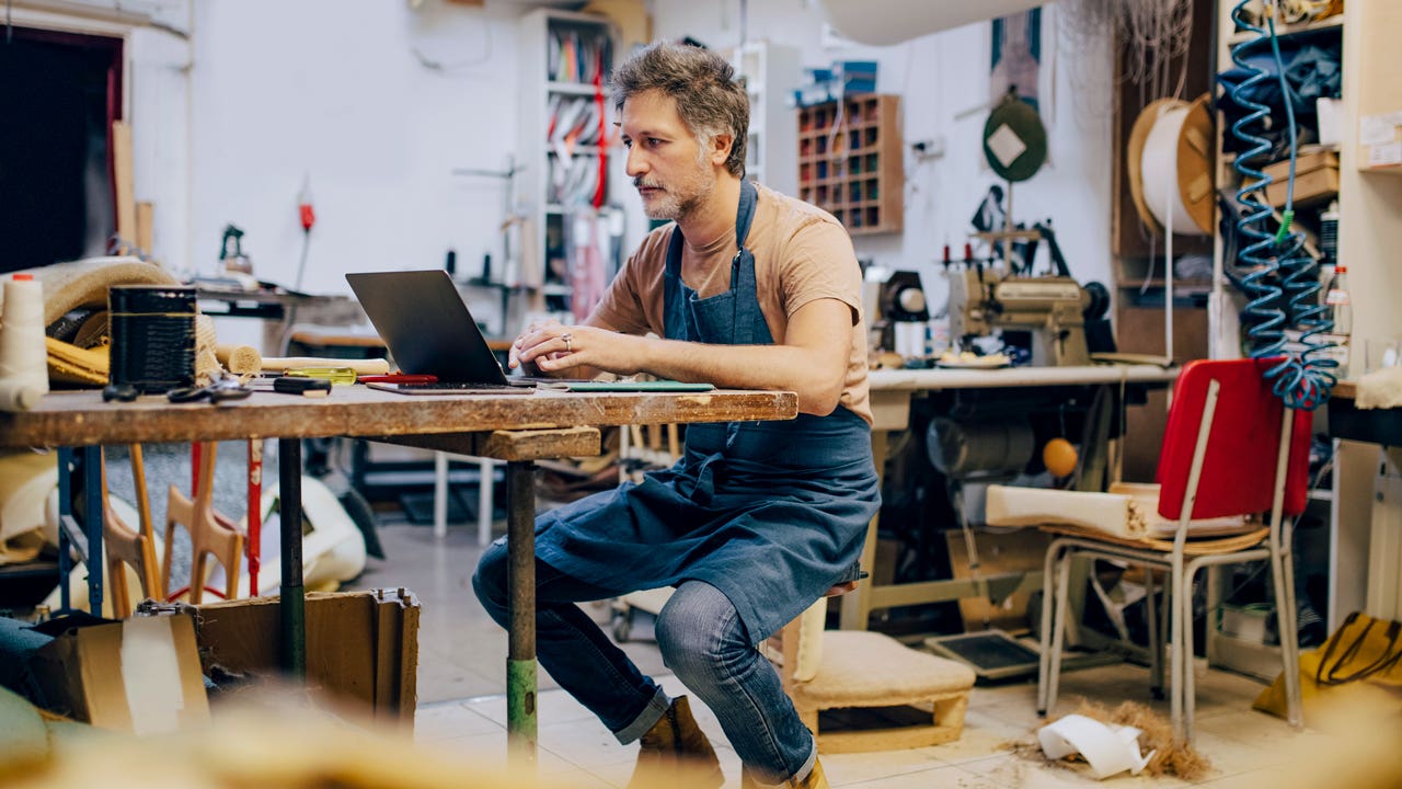 man sitting at workbench using a laptop in his workshop