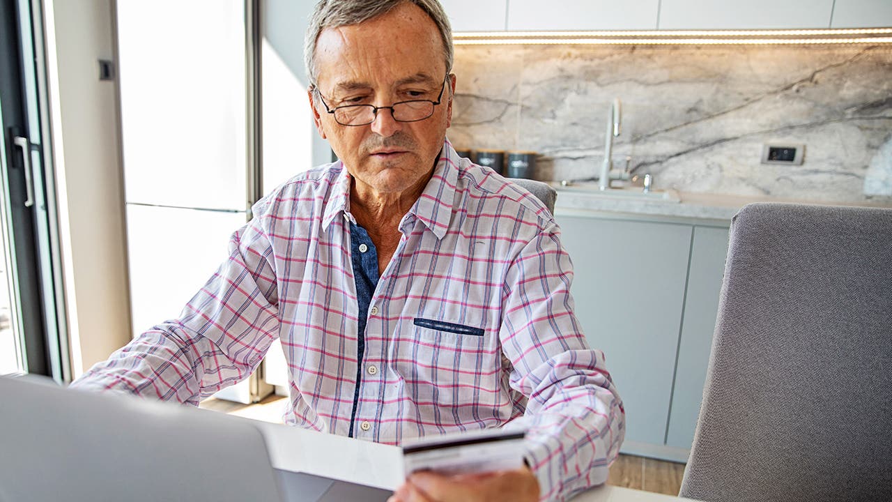 senior man online banking in home kitchen