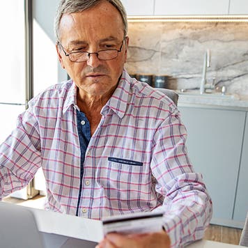 senior man online banking in home kitchen