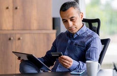 man looking at credit card while using a digital tablet