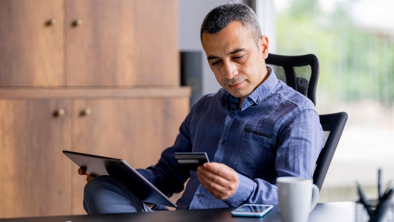 man looking at credit card while using a digital tablet