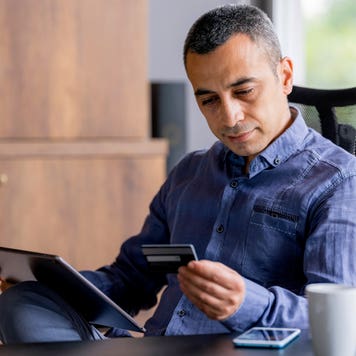 man looking at credit card while using a digital tablet