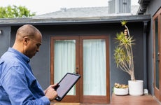 A real estate agent uses a tablet standing outside of a listing