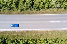 Blue car on two lane road surrounded by trees shot from above