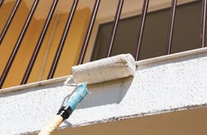 A closeup of a paint roller painting the exterior of a home