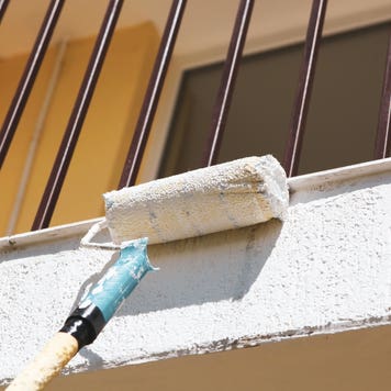 A closeup of a paint roller painting the exterior of a home