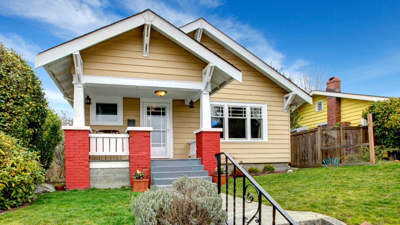 House with beige clapboard siding, red painted brick posts frame the front porch with gray stairs.