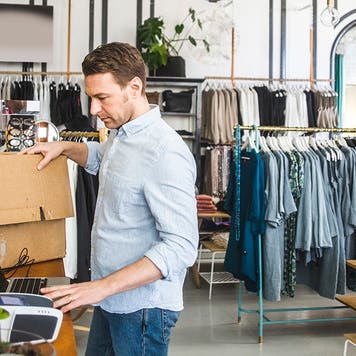 male business owner unpacking boxes in clothing boutique