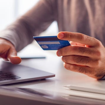 close up of hands holding a credit card and typing on computer