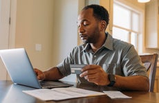 man working on laptop and holding credit card