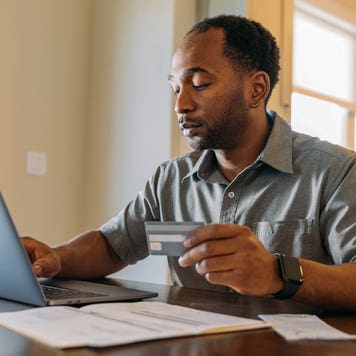 man working on laptop and holding credit card
