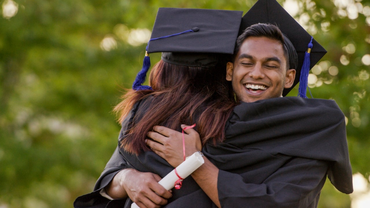 College graduate hugs another student