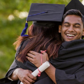 College graduate hugs another student