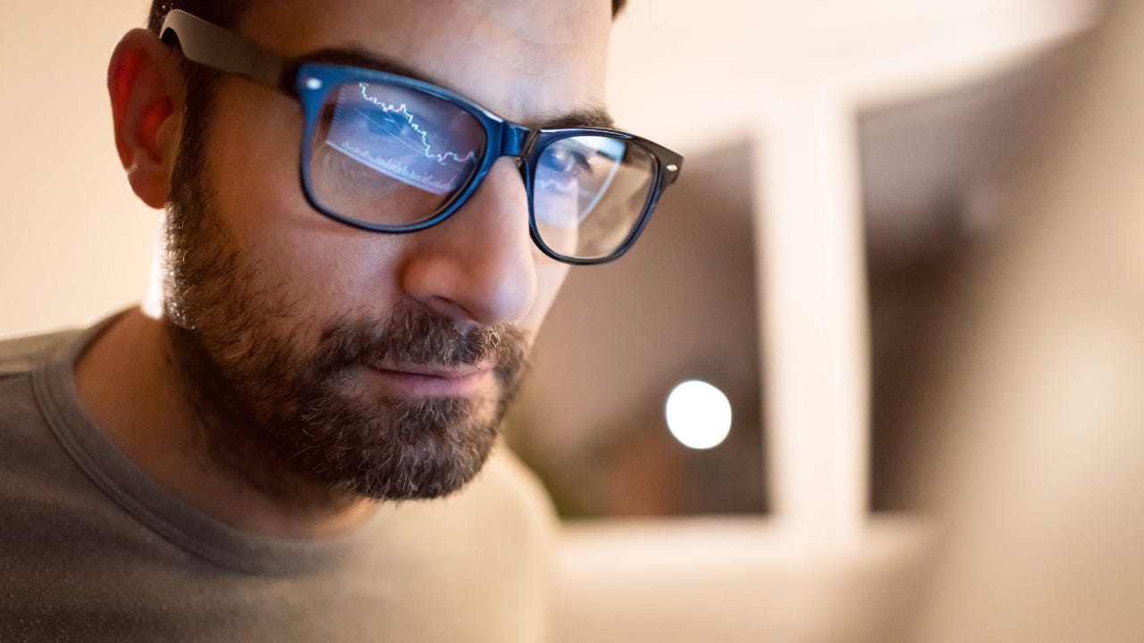 A man with glasses reflecting his trading screen