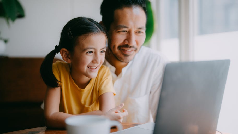 Man and child sitting at table smiling at laptop