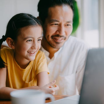 Man and child sitting at table smiling at laptop.