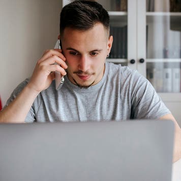 young man talking on the phone at home while using a computer