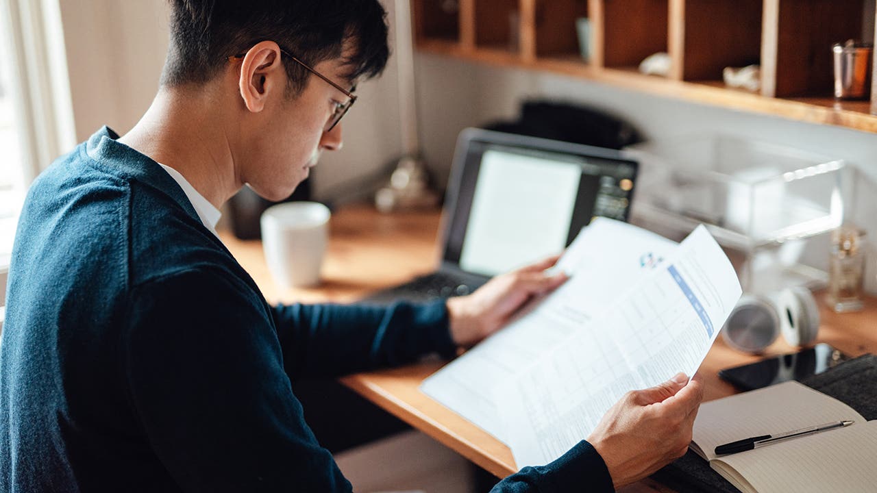 Young Asian man looking at financial bills while working on laptop at home