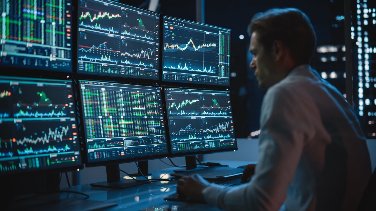 A stock trader looks on multiple trading monitors
