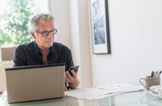 Man sitting in home office, using laptop and cell phone
