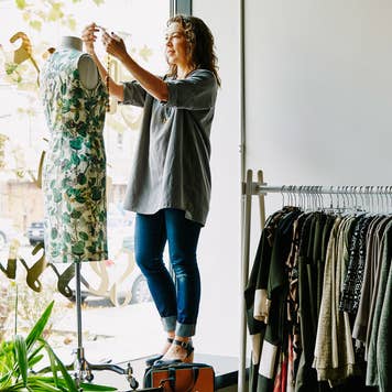 woman arranging a mannequin in her clothing store window