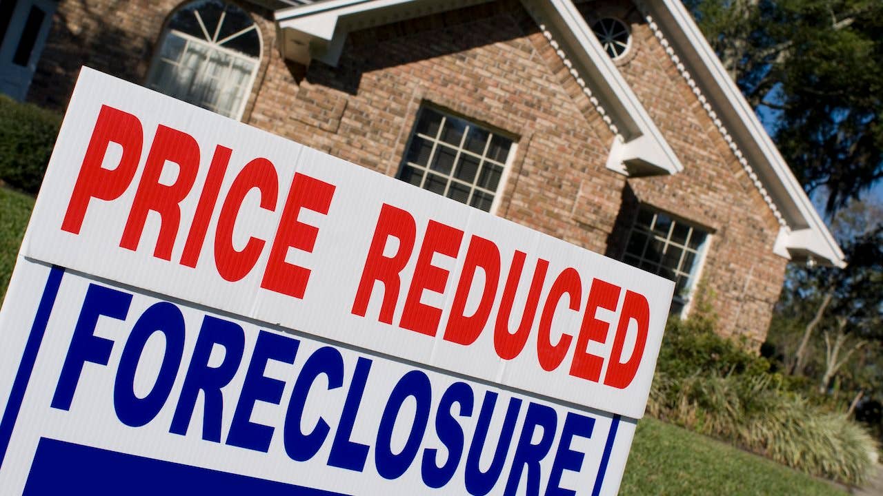 Distressed property What you should know - brick suburban home with "price reduced/foreclosure" sign in front yard