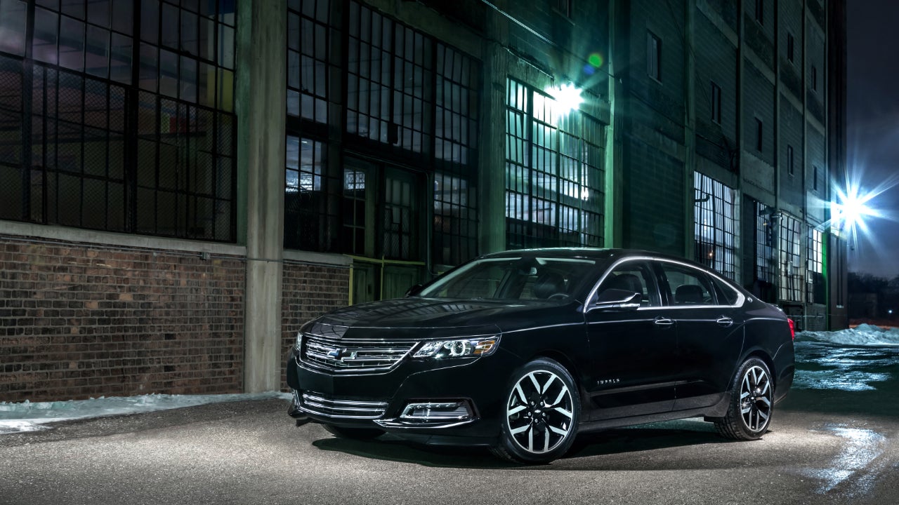 A black Chevrolet Impala parked in front of an industrial building lit in green