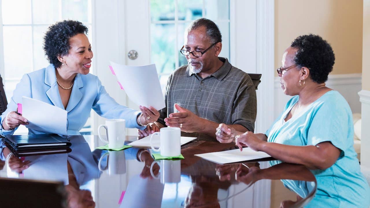What is a flat fee - older african american couple going over paperwork with a smiling african american real estate agent at the kitchen table