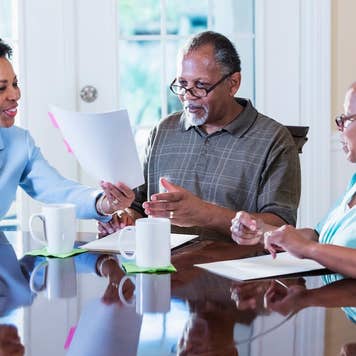 What is a flat fee - older african american couple going over paperwork with a smiling african american real estate agent at the kitchen table
