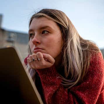 A Young University Student Laying On The Lawn Looking At Her Computer, Deep In Thought