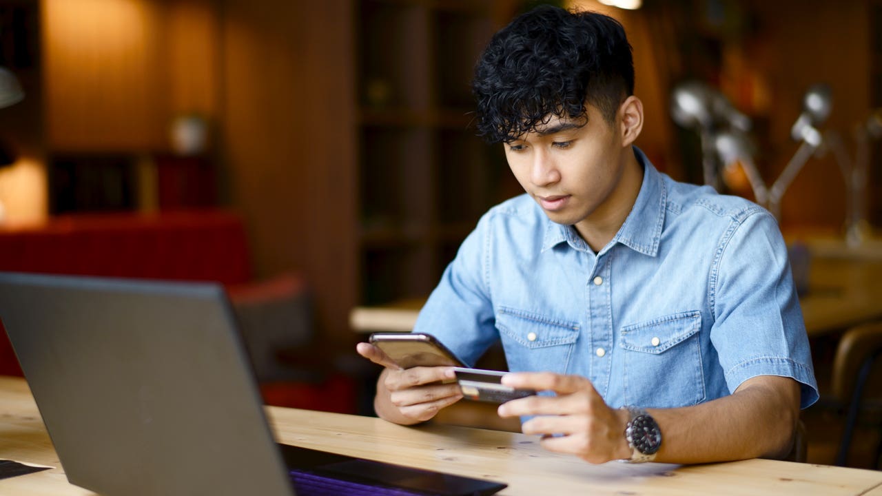 young man holding a credit card and looking at his phone