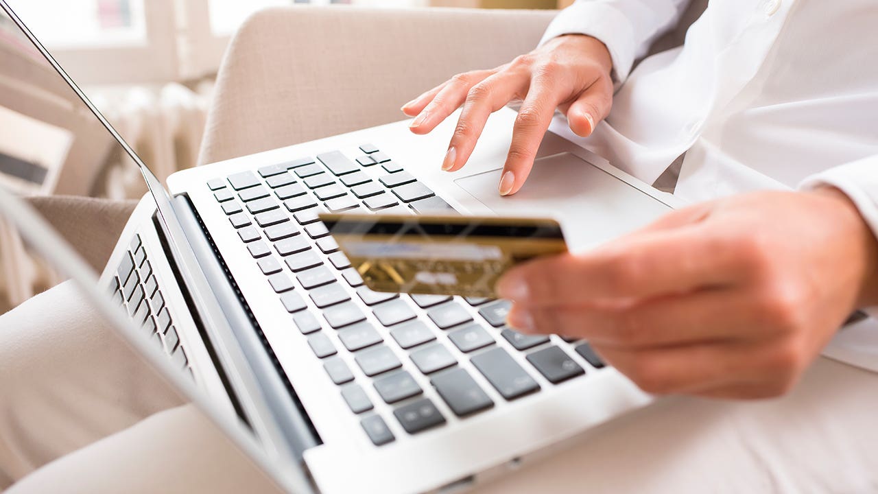 close up of a hand holding a credit card by a computer