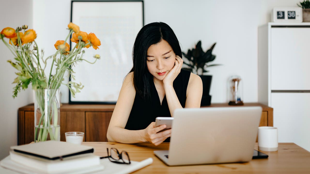 woman checking her phone and working on her laptop