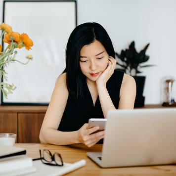 woman checking her phone and working on her laptop