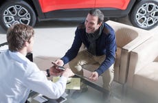 Man sitting at table in car dealership reviewing options with salesperson