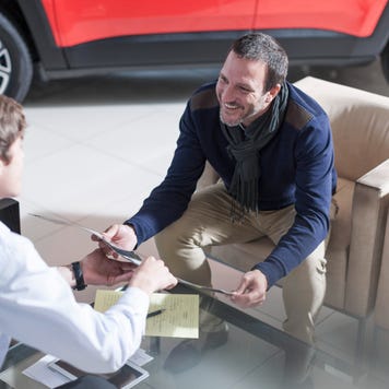 Man sitting at table in car dealership reviewing options with salesperson